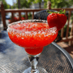 Strawberry margarita in a sugar-rimmed glass with lime and strawberry garnish on rustic wood table